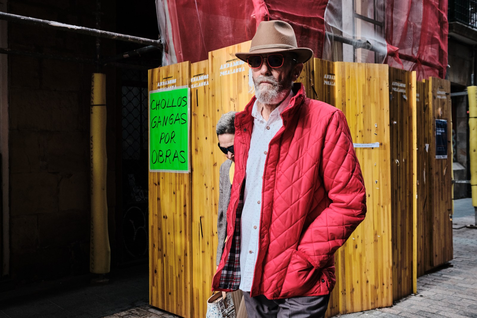 Hombre con chaqueta roja brillante paseando frente a una estructura de madera.
