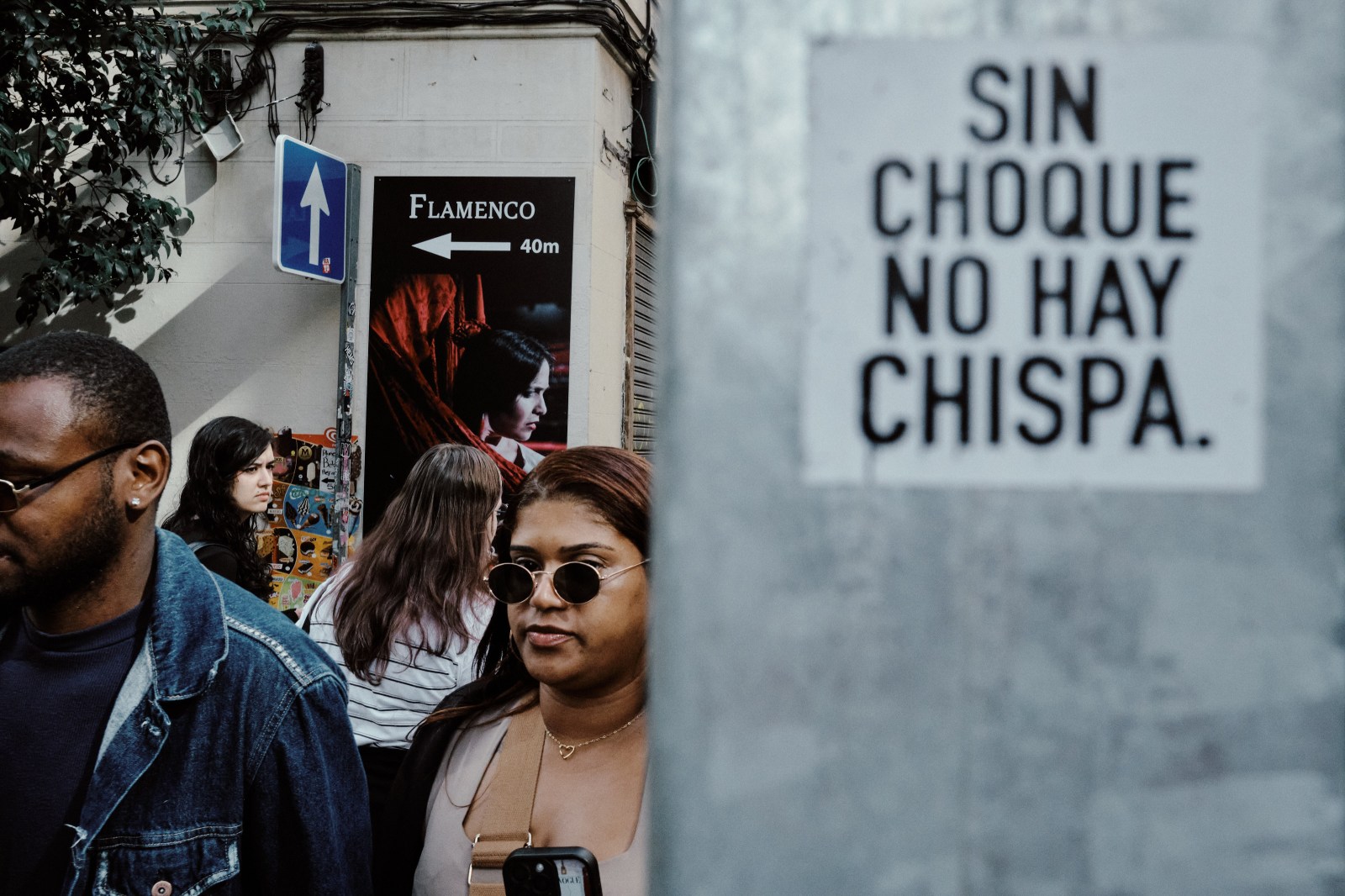 Taller de Inmersión en Fotografía de Calle en Madrid con Rober Tomás. Pegatina Sin Choque no hay Chispa y personas pasando detrás