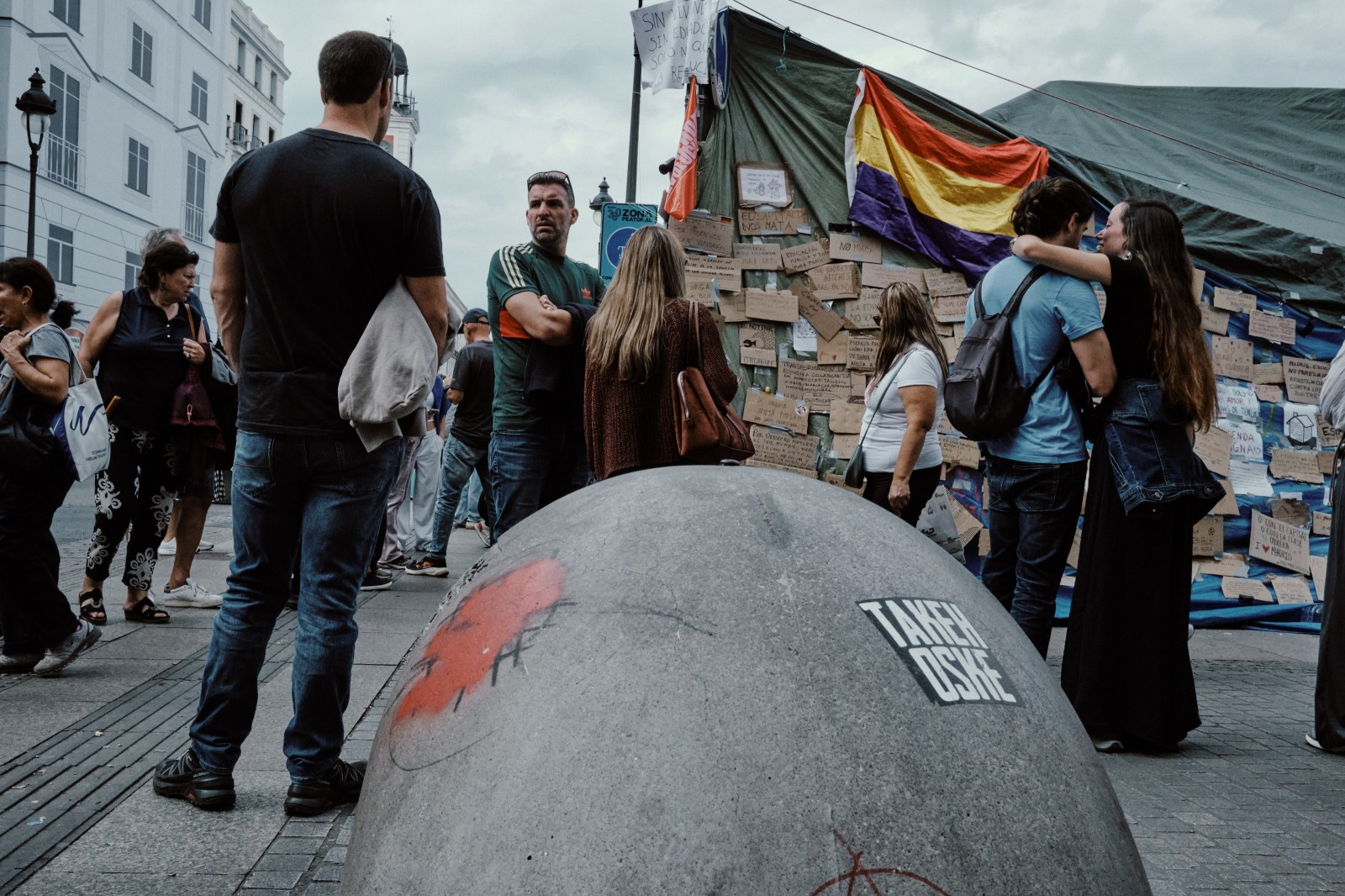 Taller de Inmersión en Fotografía de Calle en Madrid con Rober Tomás. Manifestación en Puerta del Sol para la vivienda 2026, bandera republicana y personas alrededor con actitud cariñosa