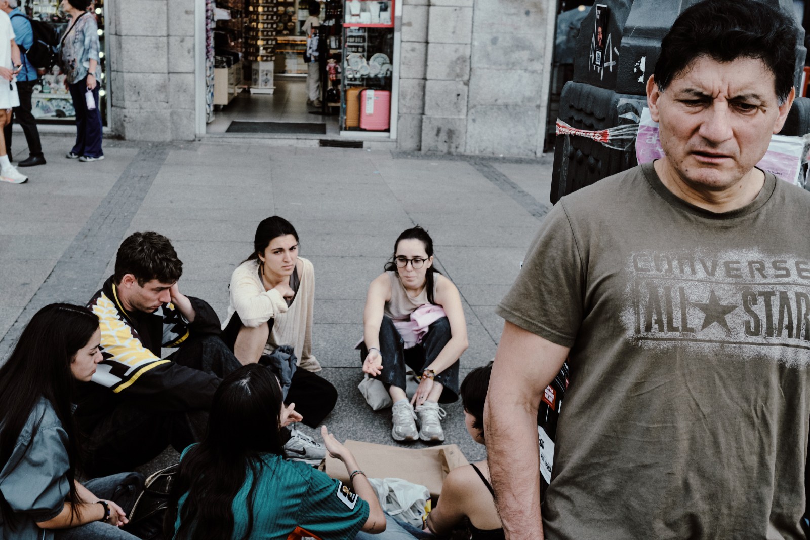 Taller de Inmersión en Fotografía de Calle en Madrid con Rober Tomás. Un hombre preocupado y al lado un grupo de chicos jovenes sentados en el suelo en la Manifestación por la Vivienda en Plaza del Sol