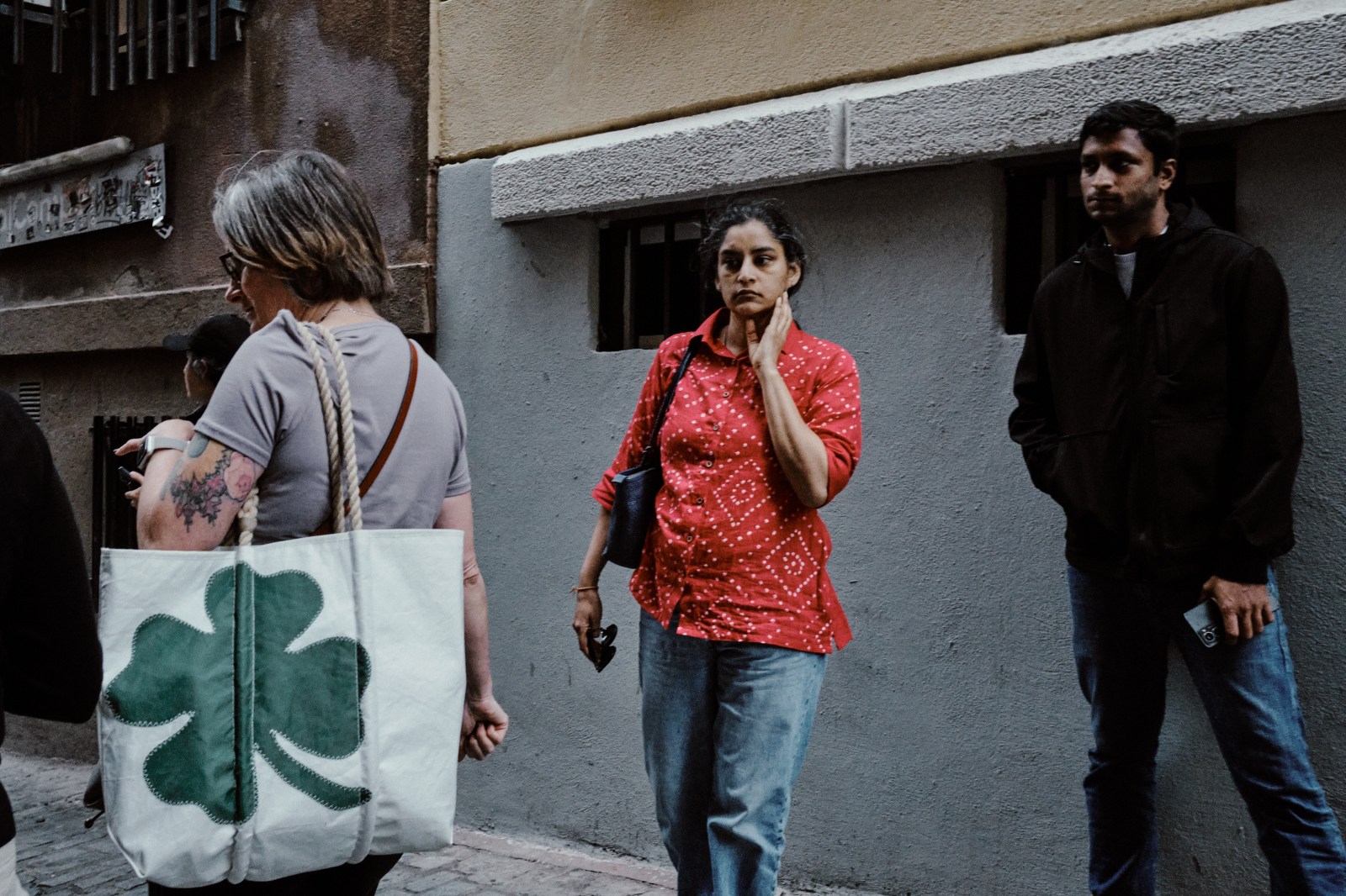 Taller de Inmersión en Fotografía de Calle en Madrid con Rober Tomás. Señora con un bolso blanco y un trébol de cuatro hojas verde pasando al lado de una pareja más pobre con camiseta roja