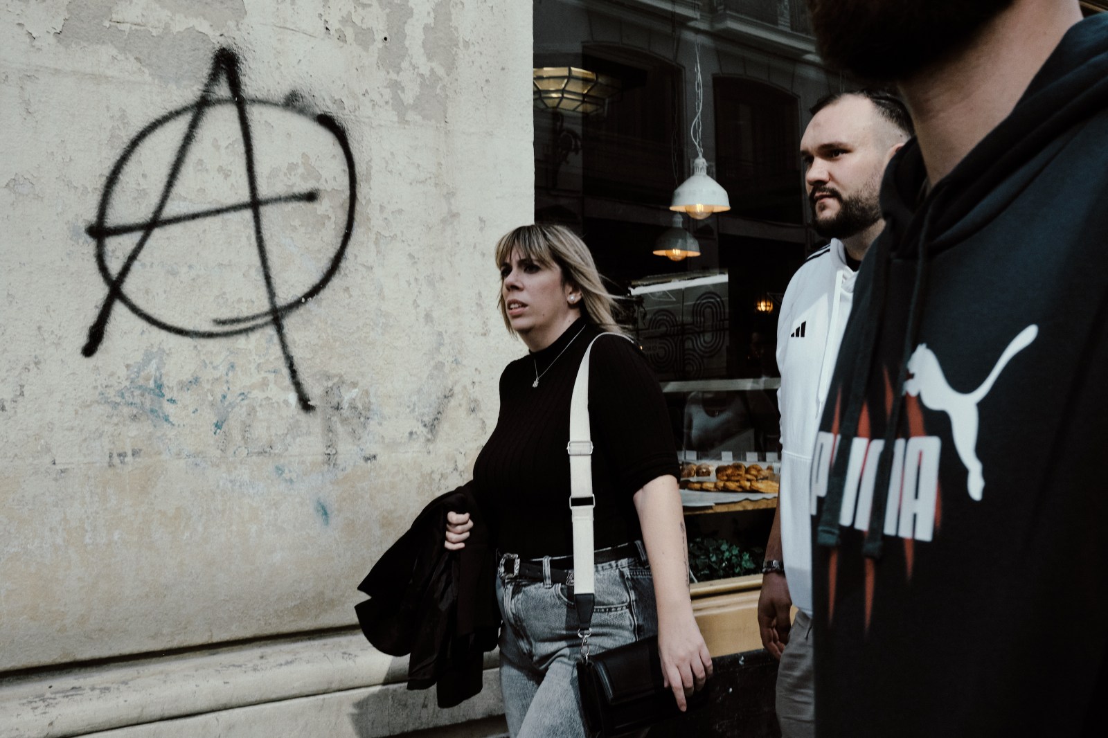 Taller de Inmersión en Fotografía de Calle en Madrid con Rober Tomás. Contraste entre marcas de ropa deportiva y simbología de anarquía en la pared