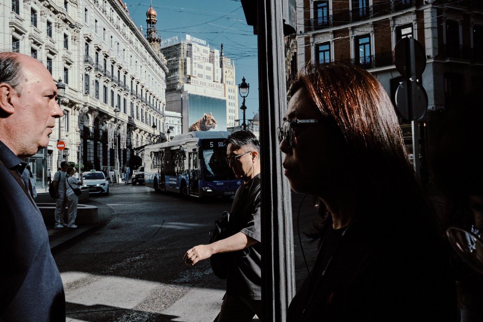 Taller de Inmersión en Fotografía de Calle en Madrid con Rober Tomás. Personas pasando por la calle y un cartel de un leopardo detrás de ellos