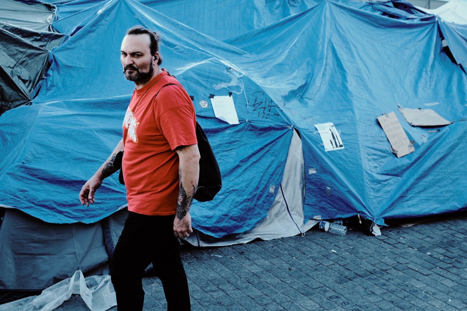 Taller de Inmersión en Fotografía de Calle en Madrid con Rober Tomás. Un hombre de rojo pasa por la acampada de Puerta del Sol por la Vivienda