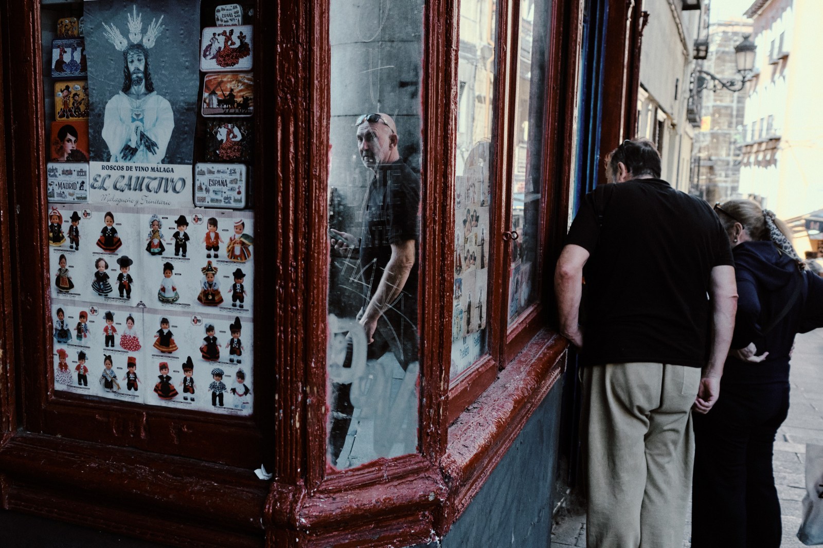 Taller de Inmersión en Fotografía de Calle en Madrid con Rober Tomás. tienda antigua con una imagen de Cristo, un espejo donde se refleja un hombre y dos personas mirando el escaparate