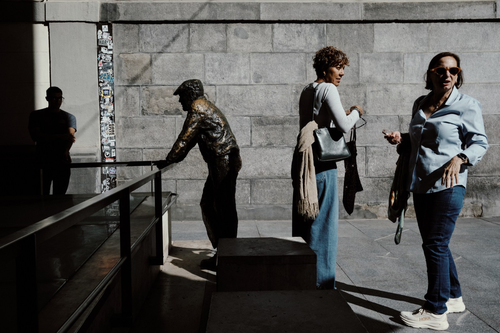 Taller de Inmersión en Fotografía de Calle en Madrid con Rober Tomás. Dos mujeres haciéndose fotos con una escultura de un hombre mayor apoyado en una barandilla